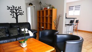 A living room with a black leather sofa, a wooden coffee table, two black armchairs, a wooden bookshelf, and a window with blinds. - Apartment with terrace and garden (Saint-Jean-de-Luz)