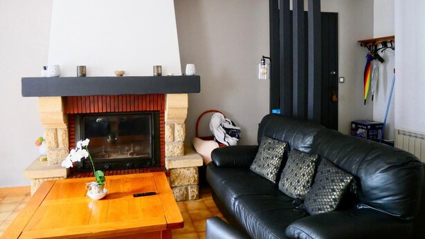A living room with a fireplace, a black leather sofa, a wooden coffee table, and a hanging lamp. - Apartment with terrace and garden (Saint-Jean-de-Luz)