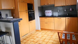 A compact kitchen with wooden cabinets, a built-in oven, a microwave, and a small countertop. - Apartment with terrace and garden (Saint-Jean-de-Luz)
