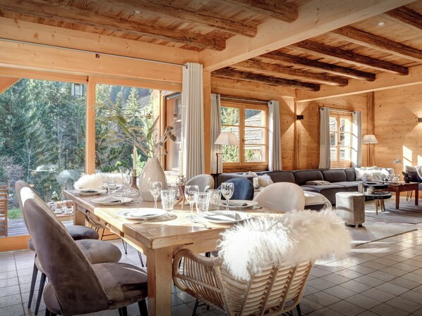 A cozy wooden cabin with a dining area, a sofa, and a view of the forest. - Chalet Hollygotty - luxury base for 8, spa, mountain views - OVO Network (La Clusaz)