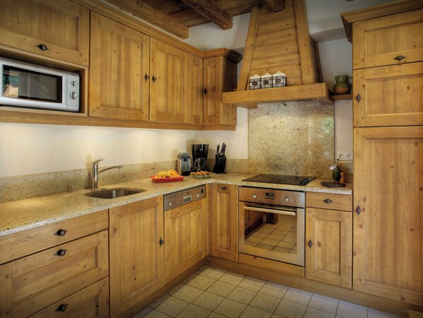 A kitchen with wooden cabinets, a microwave, a sink, a stove, and a countertop with various items. - Chalet Hollygotty - luxury base for 8, spa, mountain views - OVO Network (La Clusaz)