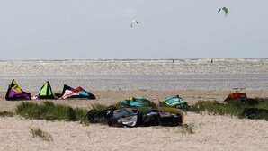 A beach with several kites and bags on the sand.