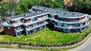 A modern multi-story building with a curved roof, large glass windows, and outdoor seating areas.