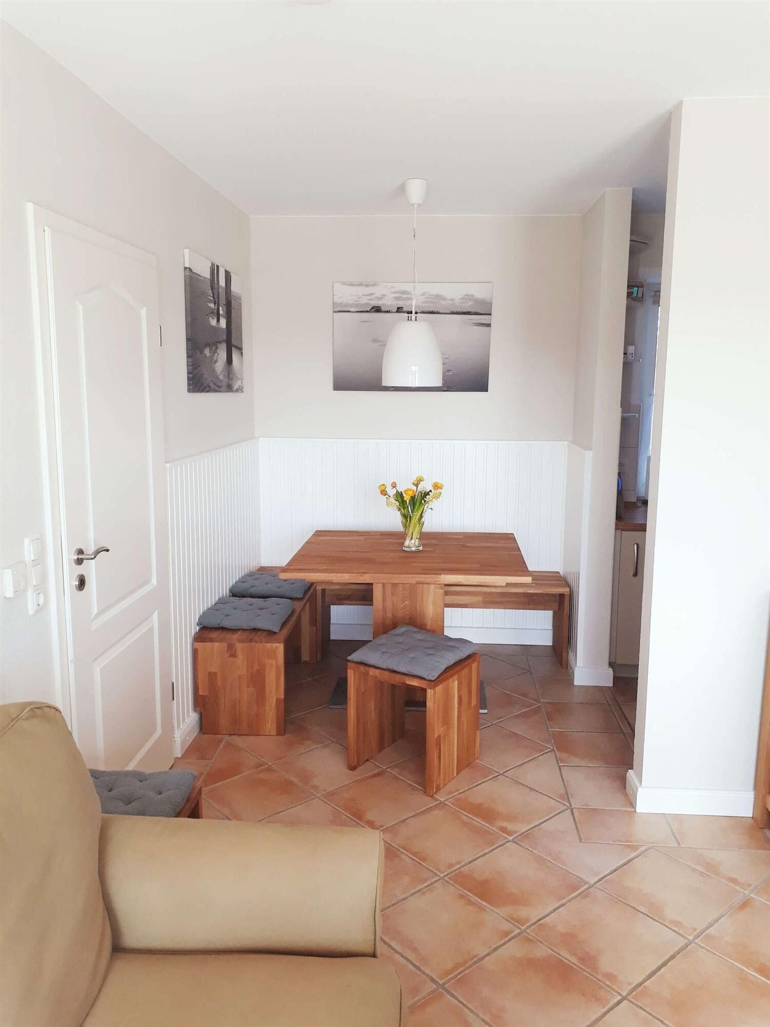 A dining area with a wooden table and benches, a white pendant light, and a view of the outdoors through a window.