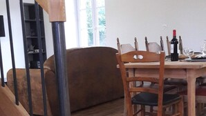 Escadaria de madeira que leva a uma sala de jantar com uma mesa posta para dois, um sofá e uma janela com luz natural.