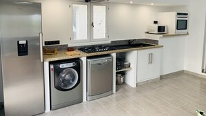 Cozinha compacta com geladeira de aço inoxidável, máquina de lavar e secadora embutidas, fogão a gás e micro-ondas.