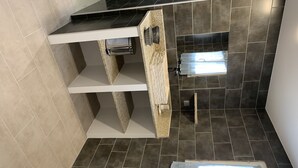 Casa de banho com azulejos escuros, sanita branca e um aparador com porta-toalhas.