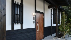 A modern building with a wooden door, black and white walls, and a small garden area. - Hinata-an (Yufu)