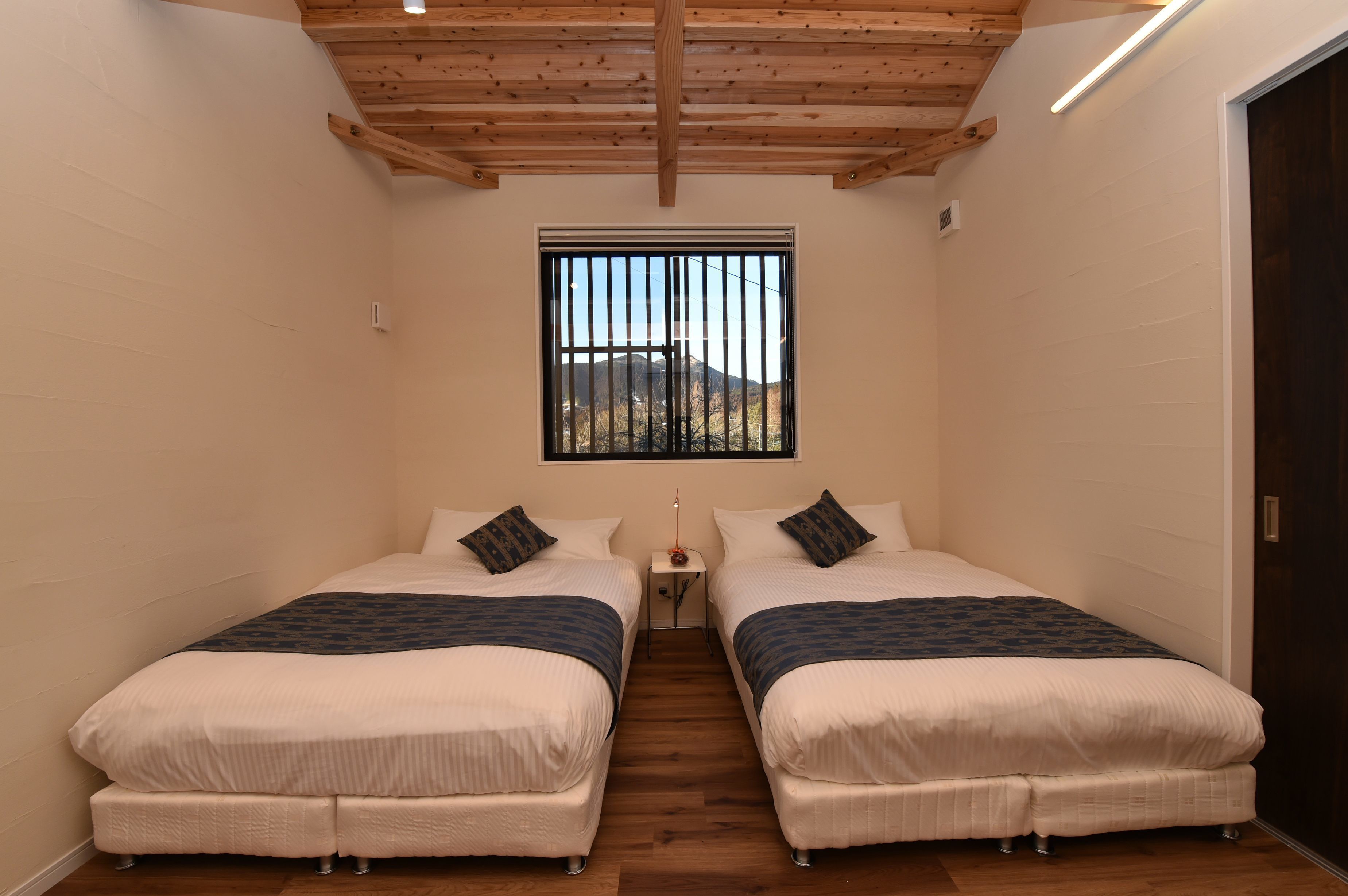 Una camera da letto piccola e luminosa, con due letti, una finestra con grate e un soffitto in legno.