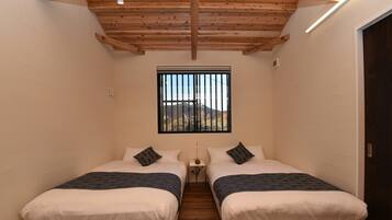 Una camera da letto piccola e luminosa, con due letti, una finestra con grate e un soffitto in legno.
