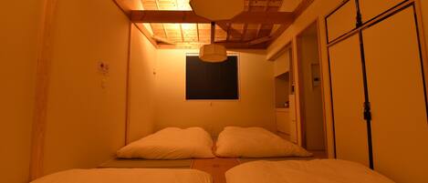 A room with two beds, a wooden ceiling, and a window with blinds.