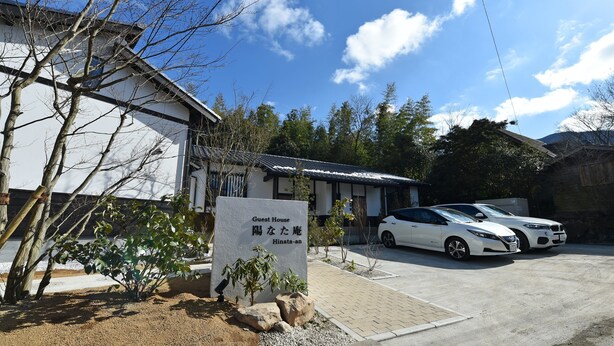 A guest house with a sign in front, two parked cars, and a clear blue sky. - Hinata-an (Yufu)