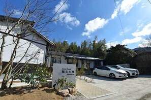 A guest house with a sign in front, two parked cars, and a clear blue sky. - Hinata-an (Yufu)