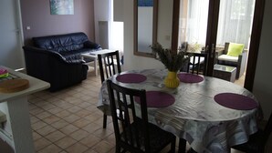 A dining area with a round table, chairs, and a black leather sofa. - Furnished holiday home with garden (Gujan-Mestras)