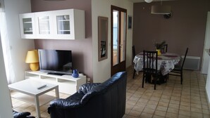 A living room with a TV, sofa, and a dining area with a table and chairs. - Furnished holiday home with garden (Gujan-Mestras)