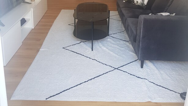Ein Wohnzimmer mit einer schwarzen Couch, einem Couchtisch, einem Fernseher und einer Küche im Hintergrund.