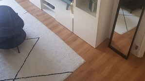 Ein Wohnzimmer mit Flachbildfernseher, einem weißen Schrank mit Dekoration, einem schwarzen Sessel und einem Spiegel.