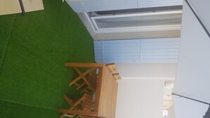 Eine Terrasse mit Holztisch und -stühlen, umgeben von einer grünen Rasenfläche und einer weißen Mauer.