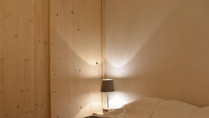 Ett rum med en säng, ett nattduksbord med en lampa och väggar som är klädda med träpanel.