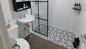 A bathroom with a white toilet, a sink, a shower enclosure, and a patterned floor. - YeoU (Mungyeong)