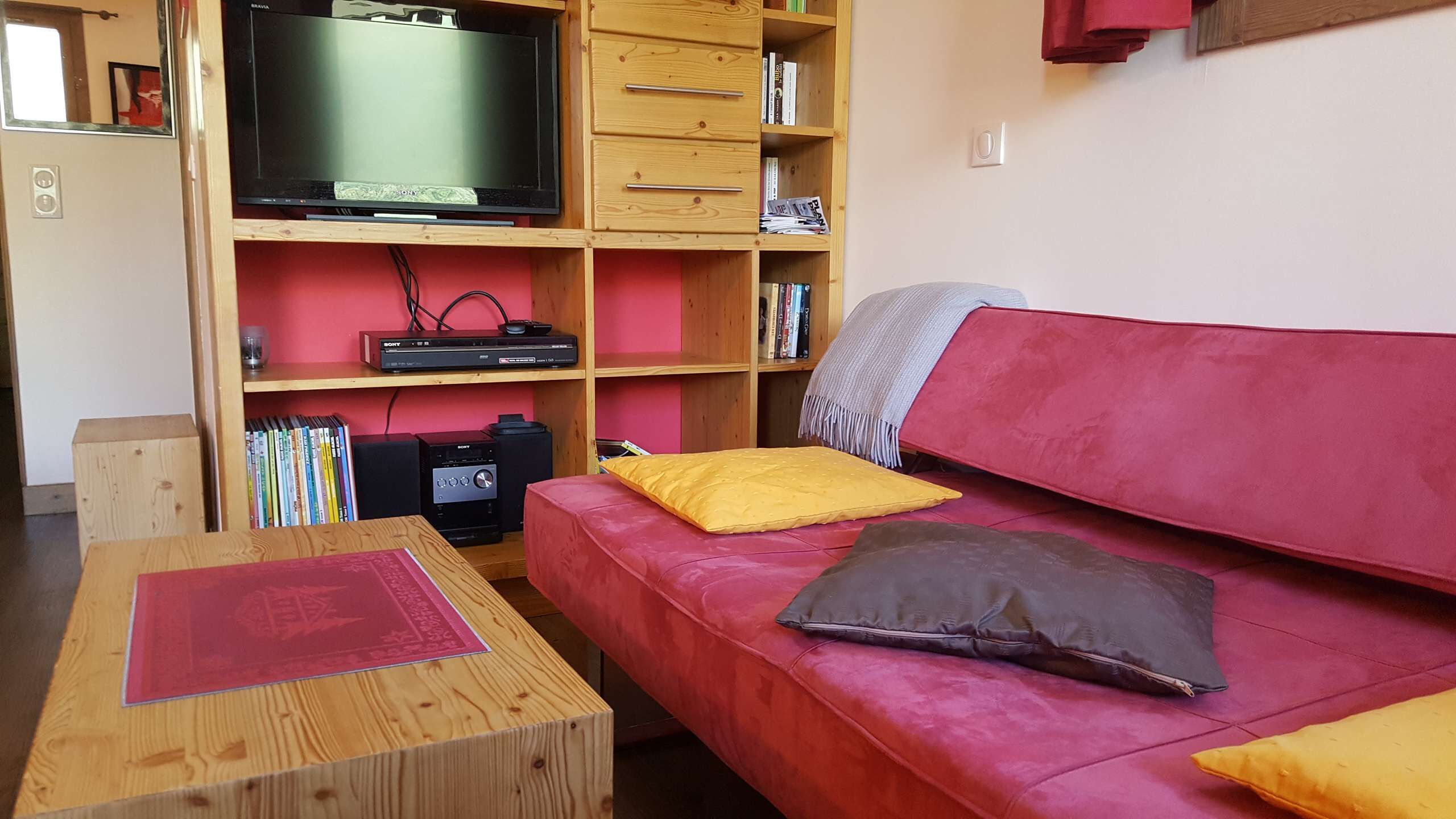 A living room with a red sofa, wooden coffee table, and a television on a wooden stand.