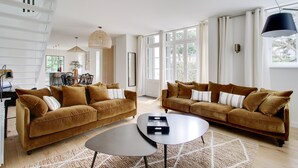A spacious living room with two brown sofas, a coffee table, and a dining area with a table and chairs.