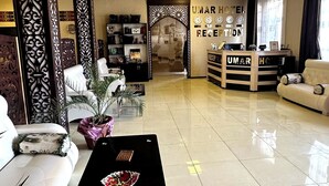 A hotel reception area with a reception desk, a waiting area with sofas, and a decorative wall with a clock. - Hotel UMAR (Khiva)