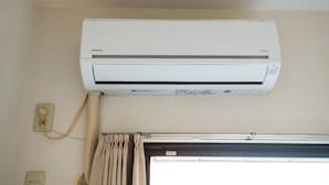 Un aire acondicionado de pared con panel de control, un enchufe y una ventana con cortinas.