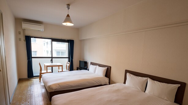 Habitación de hotel con dos camas, un escritorio, una silla y una ventana con cortinas.