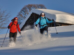 Deux personnes font du ski sur une pente enneigée, avec une structure en bois en arrière-plan.