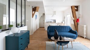 Ein modernes Wohnzimmer mit einem blauen Sofa, einer weißen Kommode und einem Essbereich im Hintergrund.