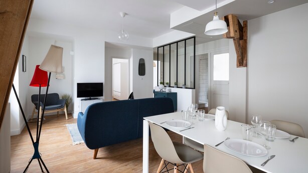 Ein moderner Essbereich mit einem weißen Tisch, gedeckt für vier Personen, einem blauen Sofa und einer roten Stehlampe.