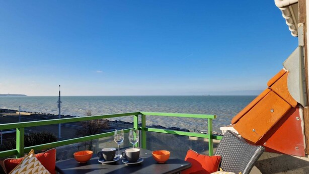 A table with a glass of water, a cup, and a bowl on a balcony overlooking the sea.