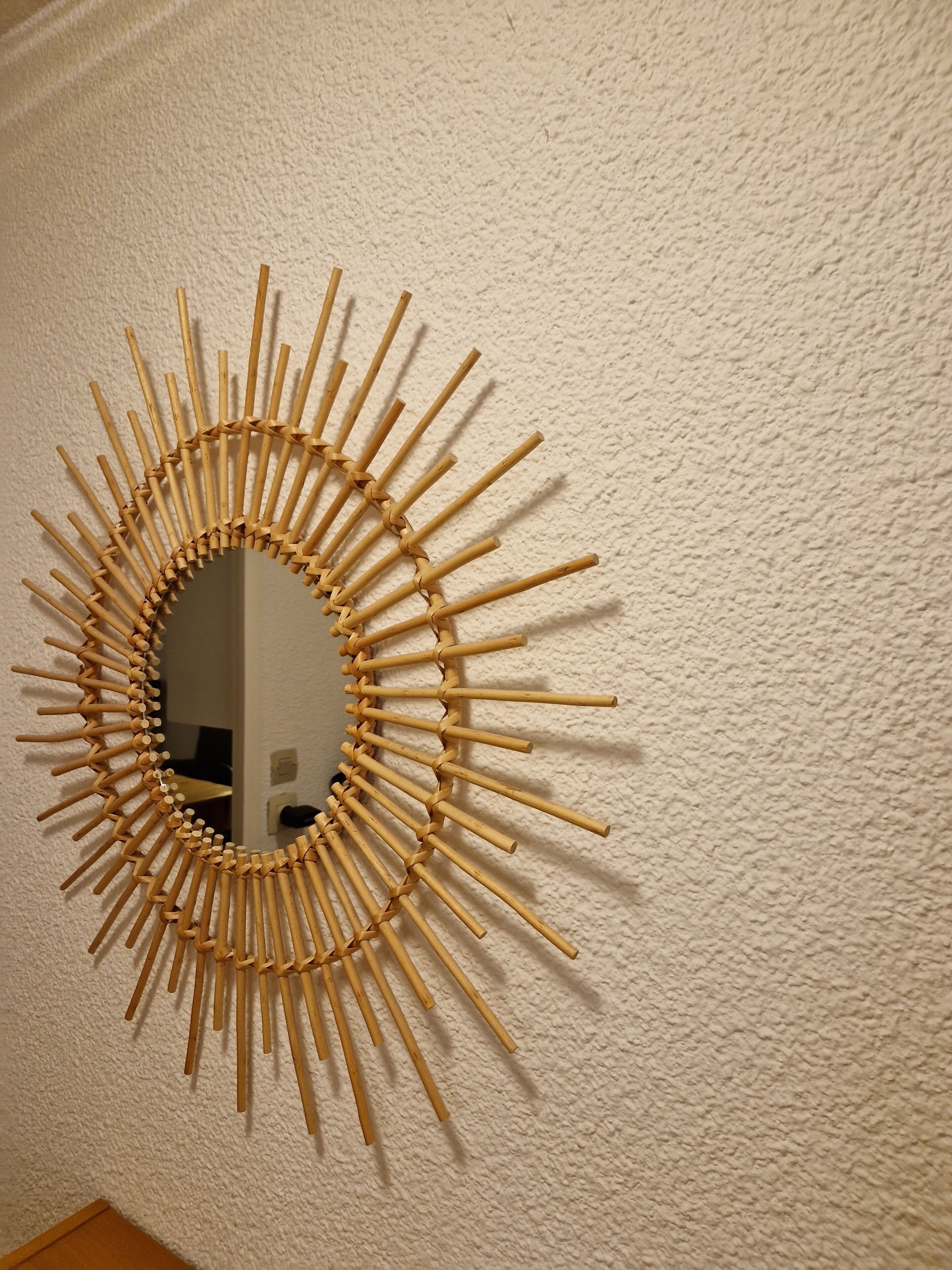 Un miroir mural orné d’un motif en forme de soleil, réalisé à partir de baguettes de bois.