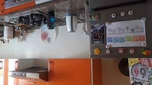 Una cocina con armarios naranja, un microondas, un hervidor y un refrigerador decorado con imanes y pegatinas.