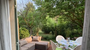 A covered patio with a cushioned seating area and a table set for dining. - La Campanette in Luberon, private pool. (Cheval Blanc)