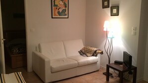 A living room with a white sofa, a small table with a TV, a lamp, and a door leading to another room. - F2 on Bordagain Hill. Ciboure (Ciboure)