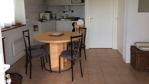 A compact kitchen with white cabinets, a microwave, and a sink. There is a dining table with four chairs and a small book on it. - F2 on Bordagain Hill. Ciboure (Ciboure)