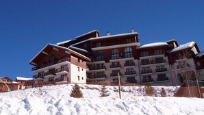 Un hôtel à plusieurs étages, doté de balcons, situé sur une pente enneigée.