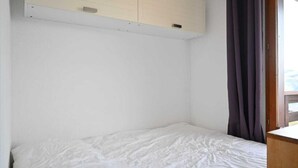 Une chambre à coucher avec un lit, une tête de lit en bois, une fenêtre avec des rideaux et un mur blanc.