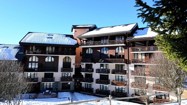 Un hôtel à plusieurs étages, doté de balcons, d’une façade en pierre et d’un toit recouvert de neige.