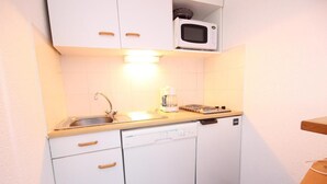 Une cuisine de taille réduite, dotée de meubles blancs, d’un four à micro-ondes, d’un évier et d’un lave-vaisselle.