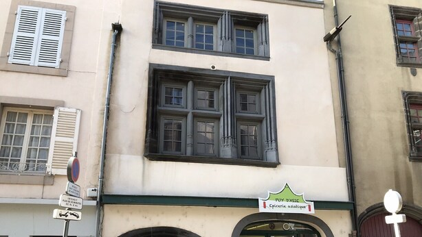 A building with a green awning, a sign reading "PUY D'ASIÈ," and a door with glass panels.