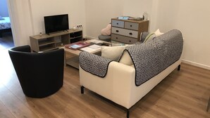 A modern living room with a sofa, a black chair, a wooden TV stand, and a small table with papers and a remote.