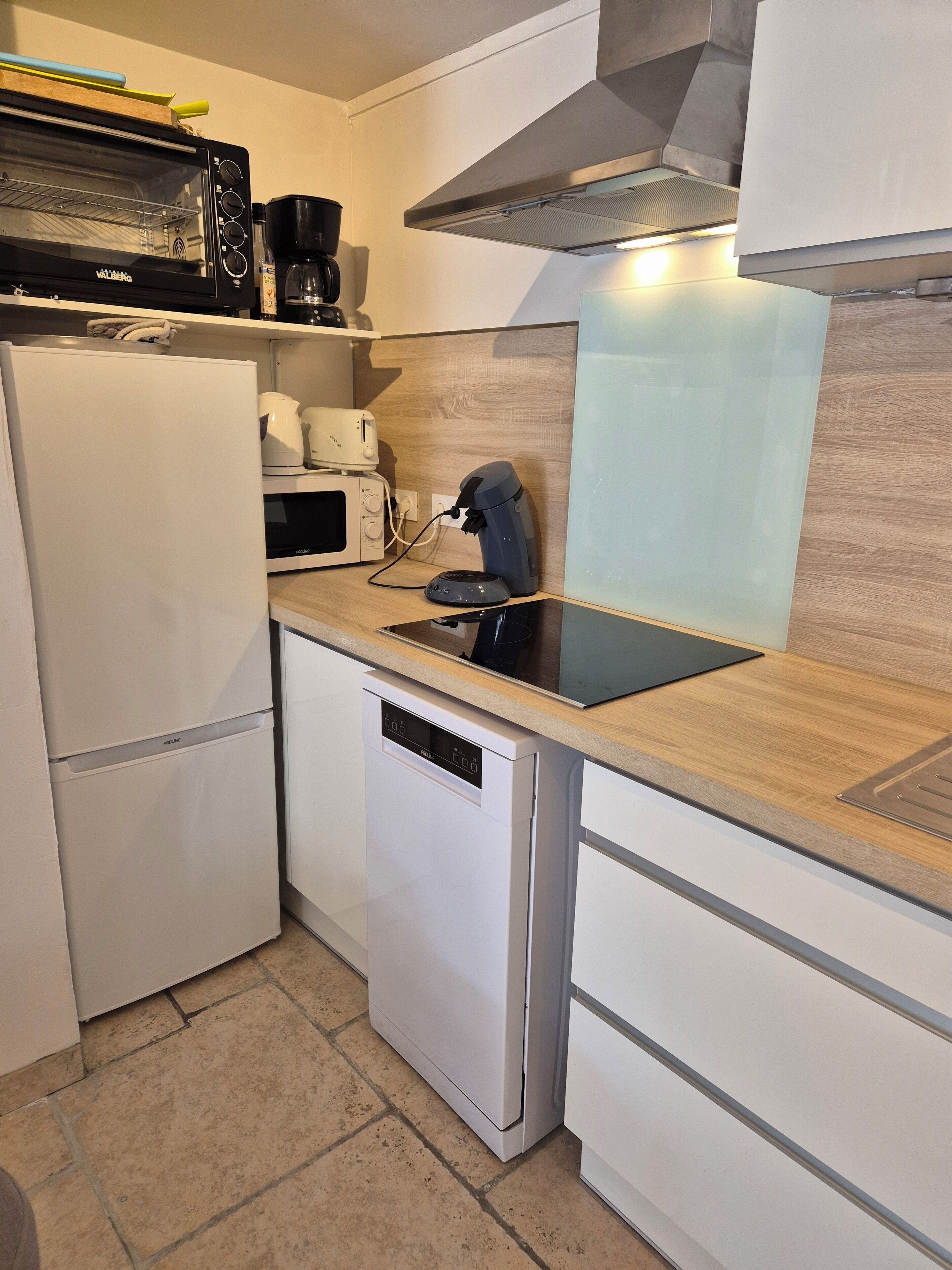 A compact kitchen with a white refrigerator, a microwave, a toaster, and a coffee maker on the countertop.