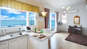 Cocina moderna con vista al mar, zona de comedor con mesa para dos y un pequeño rincón de estar con vistas.