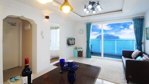 Sala de estar con vista al mar, comedor con una botella y vasos, y sofá con cojines.