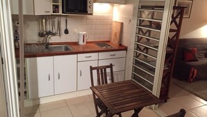 Una cocina compacta con armarios blancos, un microondas, un hervidor de agua y una mesa de madera con sillas.