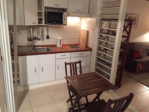 A compact kitchen with white cabinets, a microwave, a kettle, and a wooden table with chairs. - BAY VIEW MARTINIQUE! (Les Anses d'Arlet)