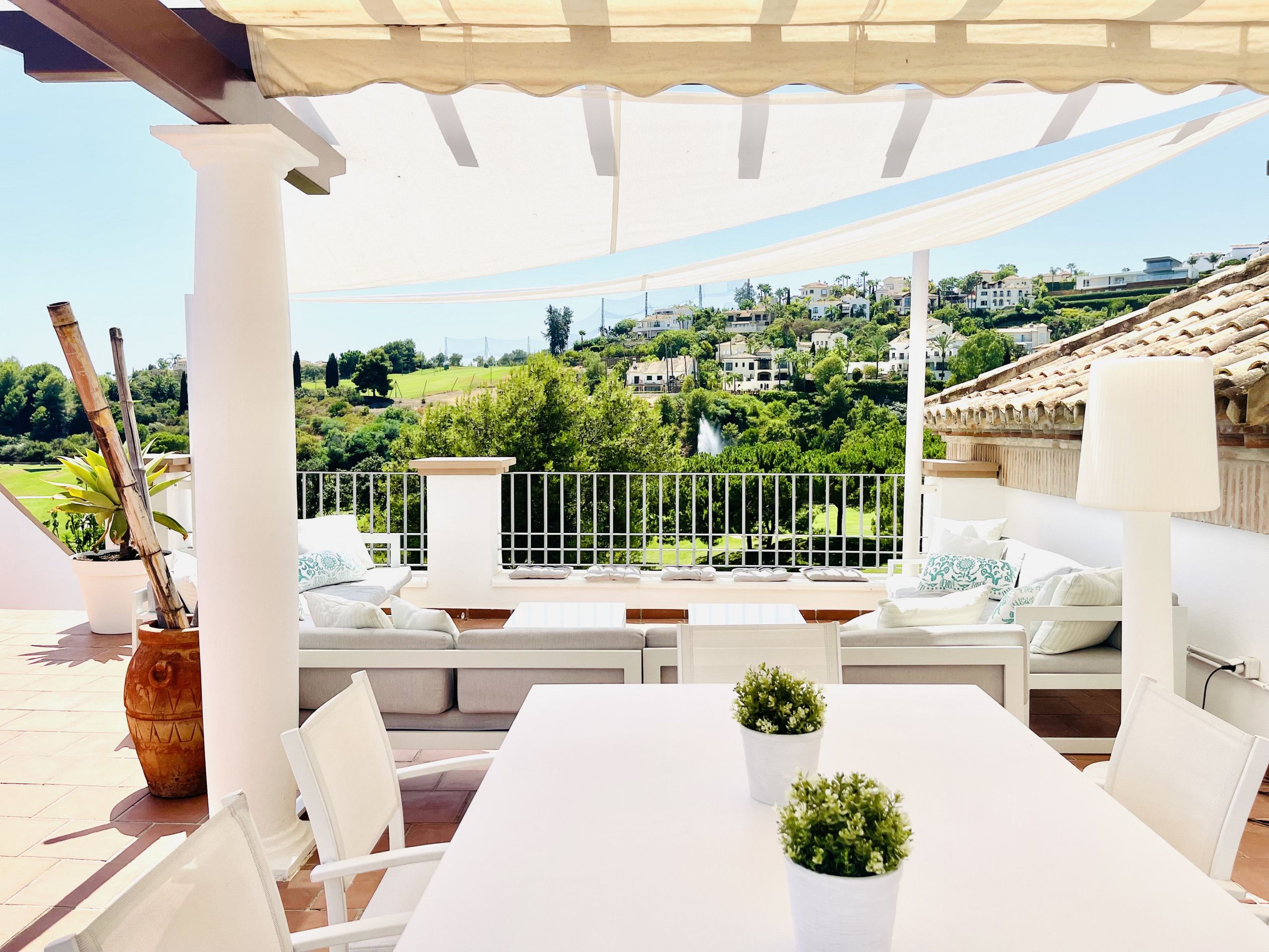 Une terrasse avec une table et des chaises blanches, un canapé et une plante en pot.